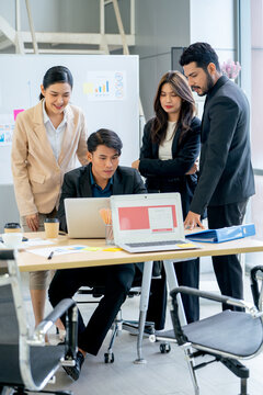 Vertical image of Asian women and man stand with young man work with laptop in the office and they look happy to success of their project.