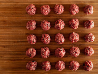 Raw uncooked meatballs on wooden cutting board.