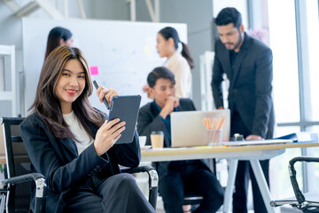 Portrait of young business woman sit on chair also hold tablet and pen with look at camera and smile in office and group of co-worker work in the back.