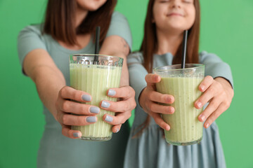Little girl with her mother holding glasses of smoothie on green background, closeup