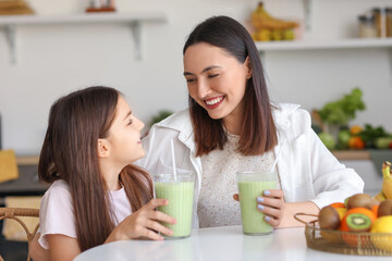 Fototapeta Little girl with her mother drinking green smoothie at table in kitchen obraz