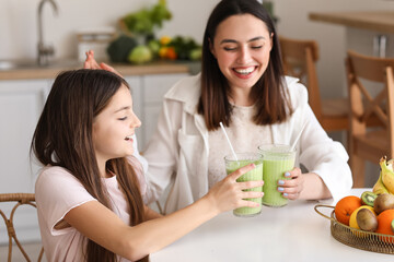 Little girl with her mother drinking green smoothie at table in kitchen