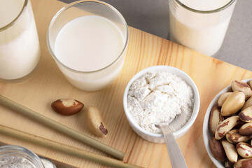 Glasses of vegan instant brazil nut milk, plate of nuts, bowl of nut flour on wooden board close up.