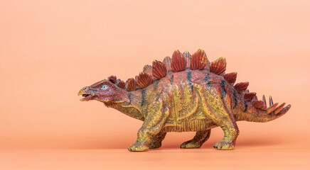 A toy dinosaur of the species Stegosaurus on an orange background