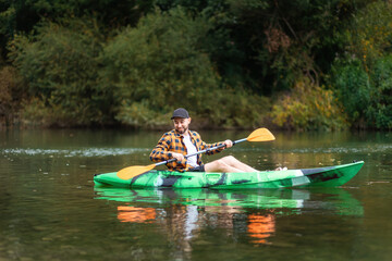 Smiling bearded caucasian man in shirt and cap kayaking at the river. The concept of water sport and activities
