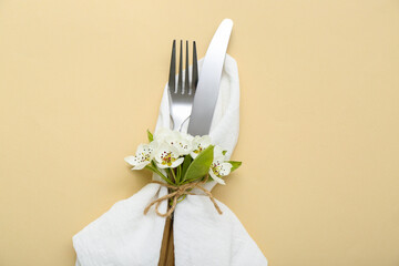 Blooming tree branch and cutlery folded in napkin on beige background