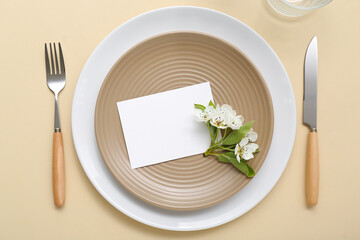 Beautiful table setting with blank invitation card and blooming tree branch on beige background