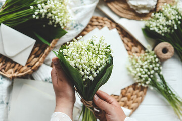 Obraz premium Girl florist holds a bouquet of lilies of the valley in her hands