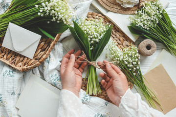 Girl florist holds a bouquet of lilies of the valley in her hands - obrazy, fototapety, plakaty