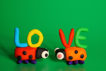 Two toy ladybugs look at each other. Next to the inscription love. Green background. Decorations for Valentine's Day.