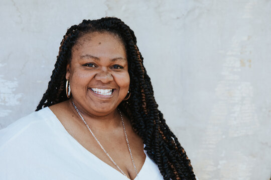 plus size afro latinx haitian american woman against white textured backdrop looking at camera smiling