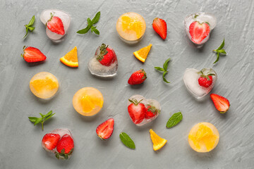 Fresh strawberry and pieces of orange frozen in ice on grey background