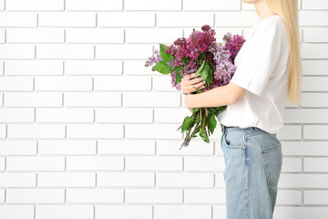 Woman holding bouquet of lilacs near white brick wall