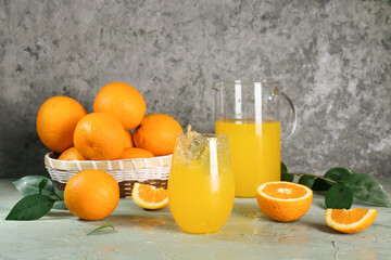 Glass of tasty orange juice with splashes and fresh fruits on grey background