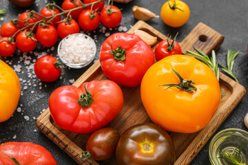 Board with different fresh tomatoes on black background