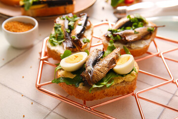 Grid of tasty sandwiches with canned smoked sprats on white tile background