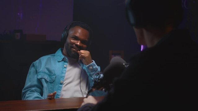 A young African-American guy speaks into a microphone on a podcast, creates a radio show or live streaming. A black man on an interview in a professional recording studio. Portrait of a male in a blog