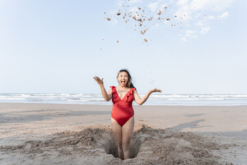 A young Hispanic woman throwing sand to the sky while making a hole playing in the beach