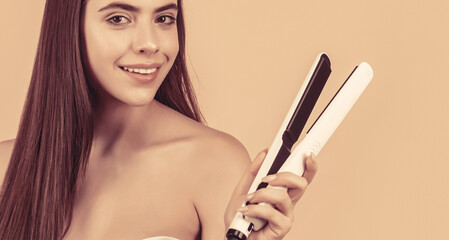 Girl using styler on her shining hair. Hairstyle. Beautiful smiling woman ironing long hair with flat iron. Woman straightening hair with straightener