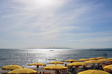 Fototapeta na wymiar Tourists lie on deck chairs under beach umbrellas in the bright sun of the summer sea