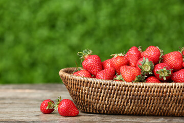 Wicker bowl with fresh strawberry on wooden table outdoors