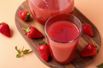 Board with jug and glass of tasty strawberry juice on orange background