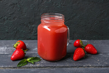 Mason jar of tasty strawberry juice on black wooden table