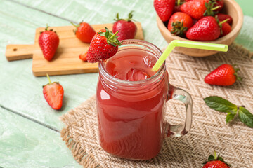 Mason jar of juice and bowl with strawberry on green wooden table