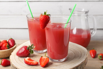 Jug and glasses of tasty strawberry juice on wooden table