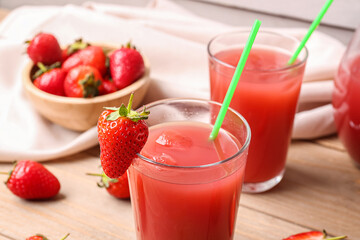 Glasses of juice and bowl with strawberry on wooden table