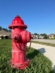 Fototapeta na wymiar red fire hydrant on the street with green grasses, blue sky and beautiful houses in the landscape