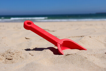 Small toy shovel in the beach sand, with ocean waves in the background.