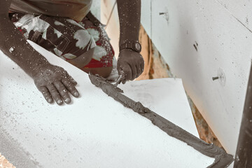 Installing white polystyrene heat insulation, detail on worker hand putting gray bonding cement glue on white boards