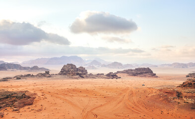 Fototapeta na wymiar Red orange Mars like landscape in Jordan Wadi Rum desert, mountains background overcast morning, small vehicle distance for scale. This location was used as set for many science fiction movies