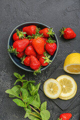 Bowl with ripe strawberry, lemon and mint on dark background