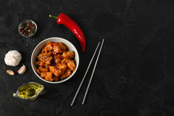 Tasty sweet and sour chicken in bowl with spices on dark background