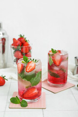 Glasses of fresh strawberry mojito on light tile table