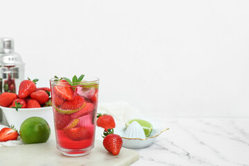 Glass of delicious strawberry mojito on light background