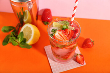 Glass of fresh strawberry mojito with straw and shaker on orange table near pink wall