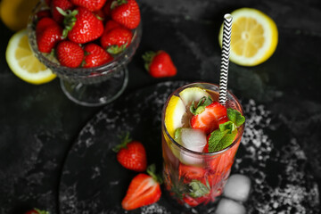 Glass of fresh mojito and bowl with strawberry on grunge black background