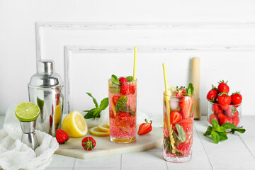 Glass of fresh strawberry mojito with shaker and jigger on white tile table