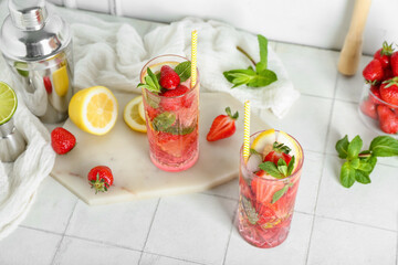 Glass of fresh strawberry mojito with shaker and jigger on white tile table