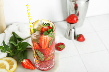 Board with glass of fresh strawberry mojito, jigger and shaker on white tile table