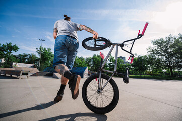 Back view of an extreme urban middle-aged bike rider falling off his bmx bike in a skate park.