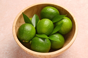Bowl with fresh limes and leaves on pink background