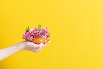 Child’s Hand Holding Croissant With pink Flowers . Summer banner with croissant. Creative cover  for summer or spring menu.