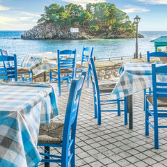 Traditional tavern restaurant with empty tables and chairs in front of Panagia island in Parga, Greece, Europe.