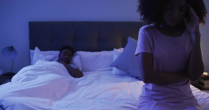 Infertility, depression and a black woman worried on the bed with her husband sleeping at night. Cheating, affair or infidelity or sleepless with a girlfriend feeling sad in the bedroom of her home