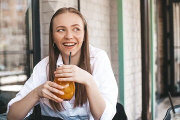 Close-up of young caucasian woman enjoying drinking orange lemonade sitting in cafe. Blonde in...