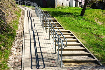 Outdoor paved stairway in hilly village with wheelchair lane and handrail for disabled persons